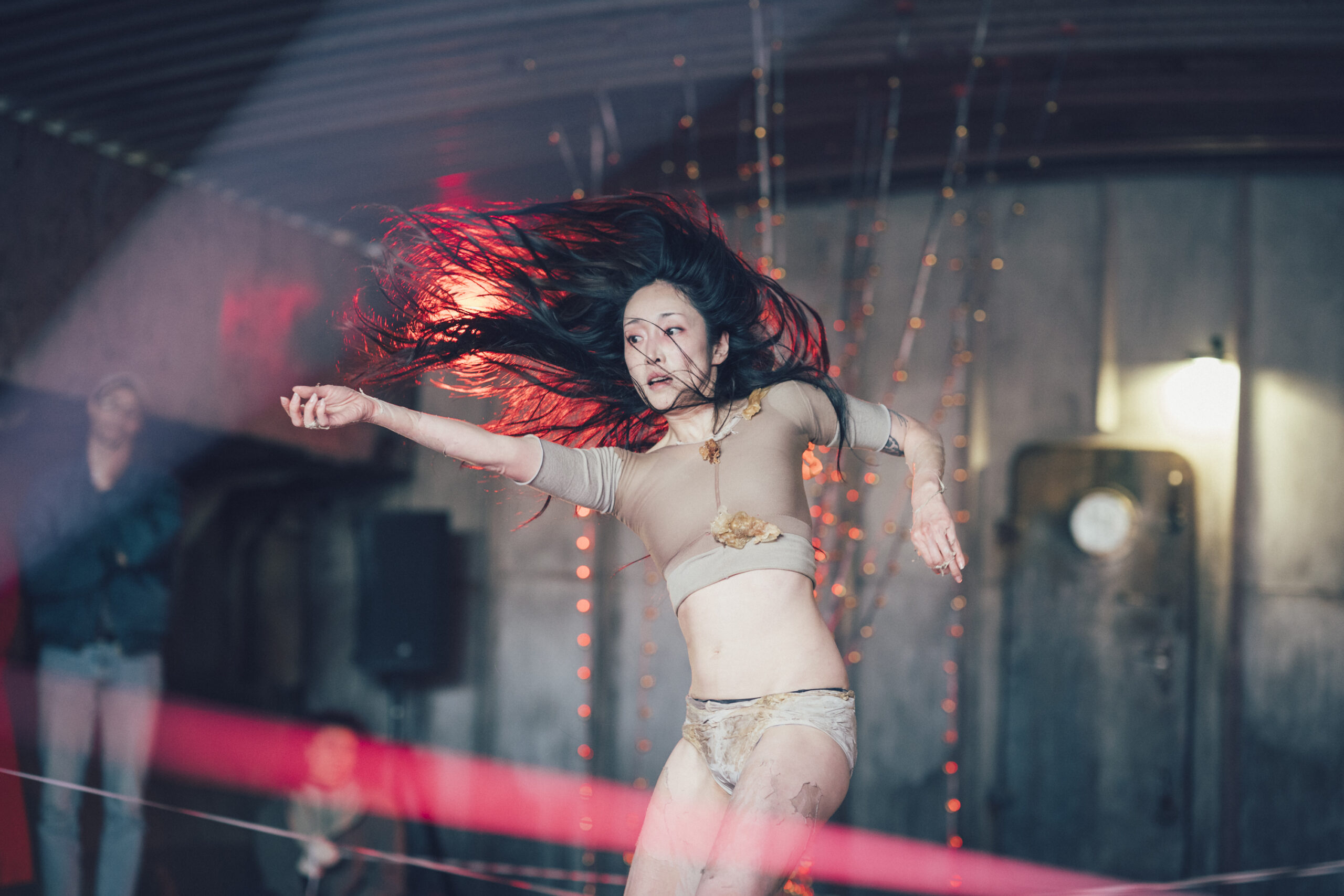 A person dancing in a wide space. They are wearing a nude coloured costume